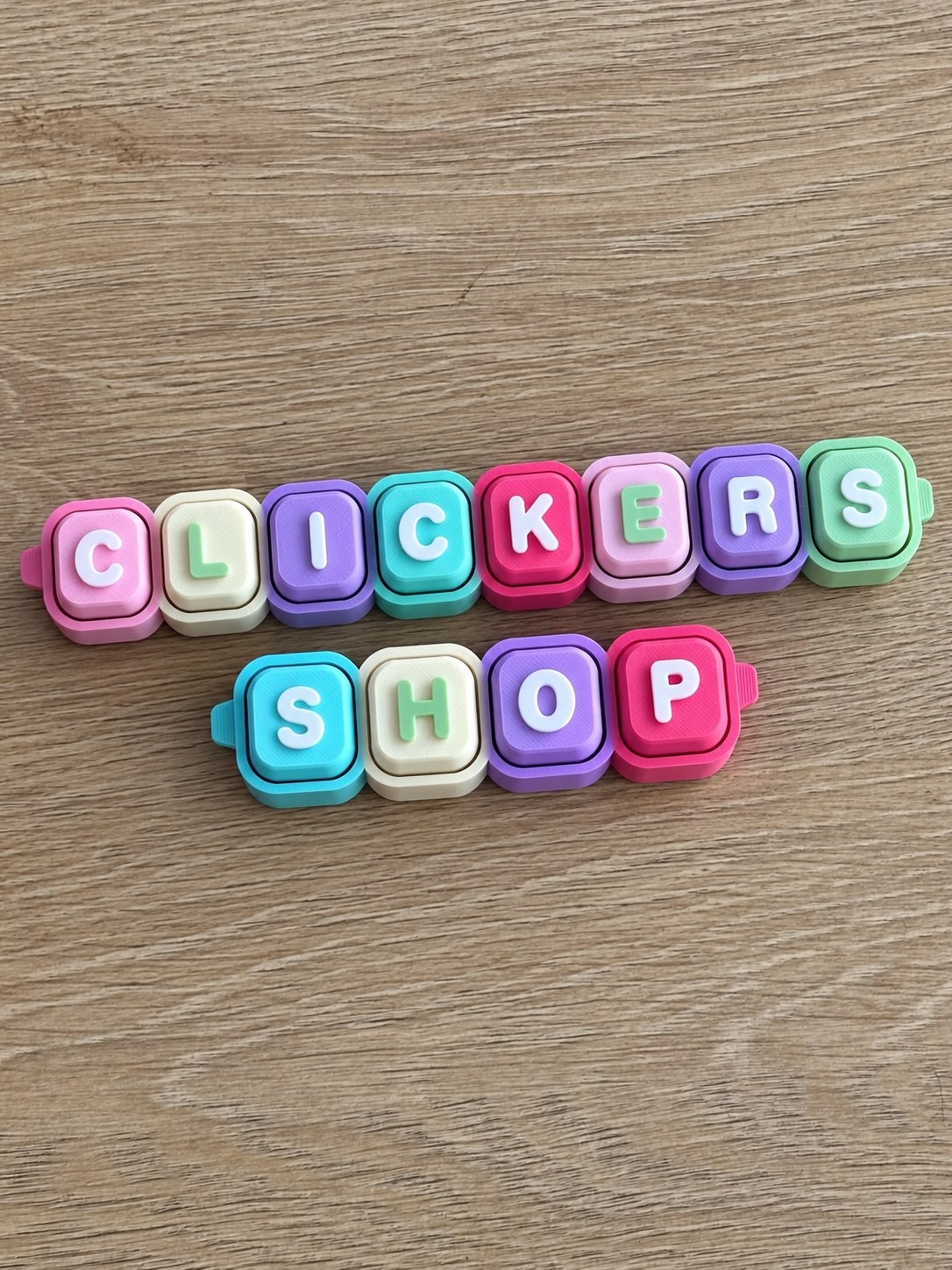 Pastel letter clickers arranged to spell CLICKERS SHOP on a wooden tabletop
